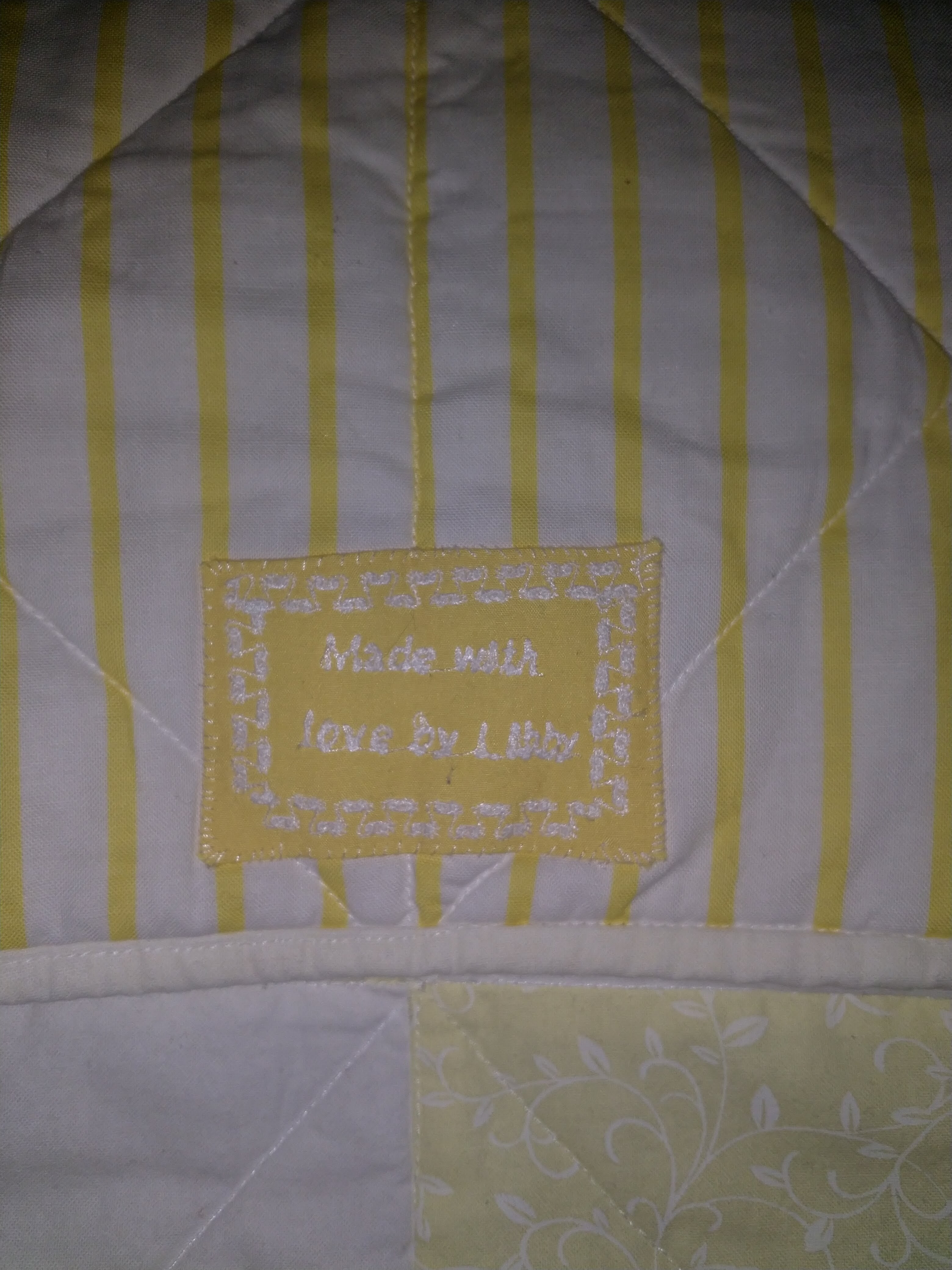 Fabric label machine embroidered with the words "Made with love by Libby" on a yellow and white striped quilt